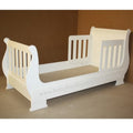 White toddler bed with beige mattress on a brown background