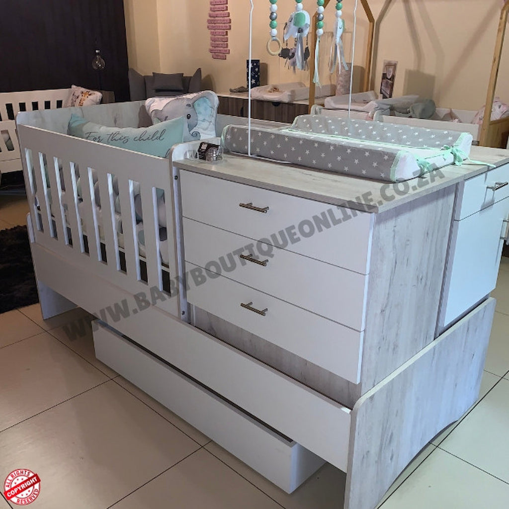 White baby crib with drawers and changing table in a showroom setting.