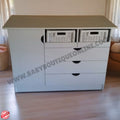 White dresser with drawers and baskets on top in a room setting.