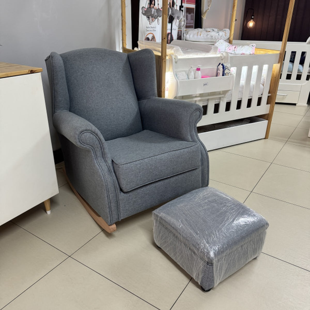 Gray armchair with matching ottoman on a tiled floor in a store setting.