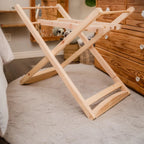 Wooden folding laundry rack on a carpeted floor with wooden furniture in the background